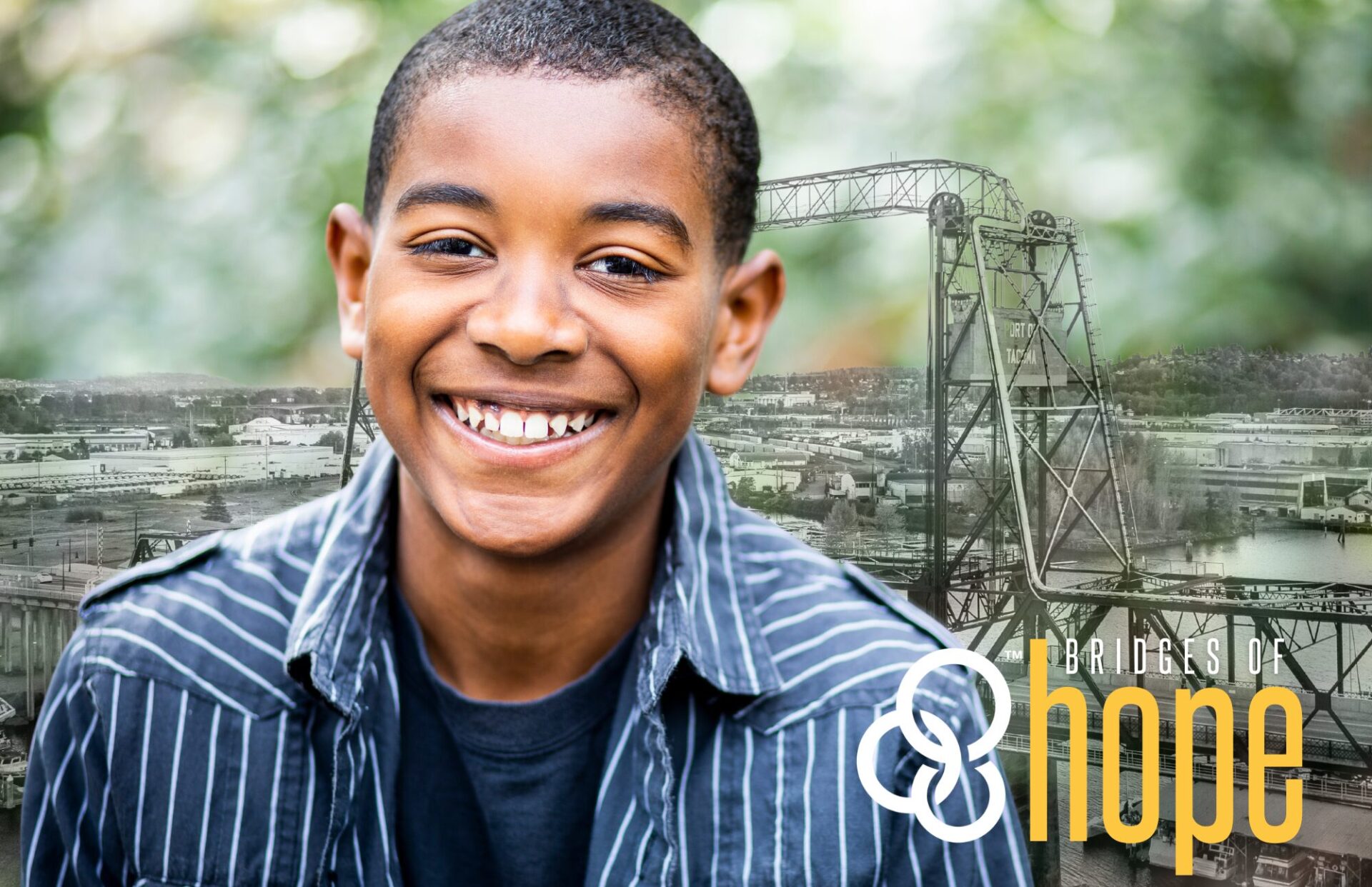 Collin, a young teenage boy in a blue striped shirt, smiles in front of a faded image of Murray Morgan Bridge