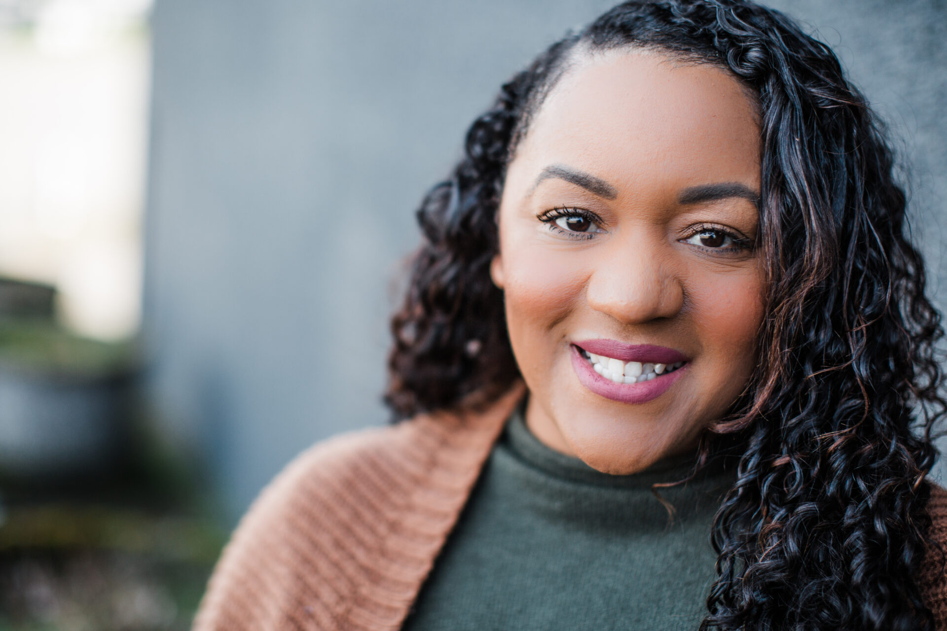 Cecily Crosbey, Tacoma Area Youth for Christ Development Director, wearing a green sweater with a brown cardigan in front of a gray wall, is smiling at the camera.